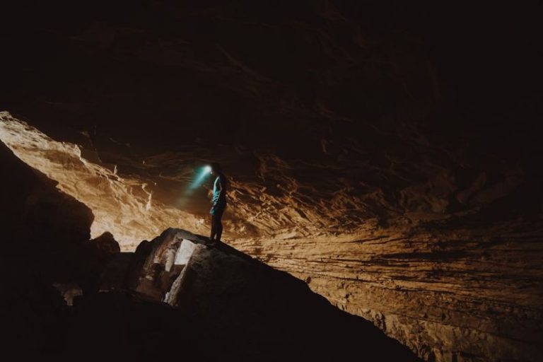 Caving - person in blue jacket standing on brown rock formation during daytime