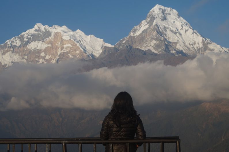 Mountain Treks - a woman standing on a balcony looking at a mountain range